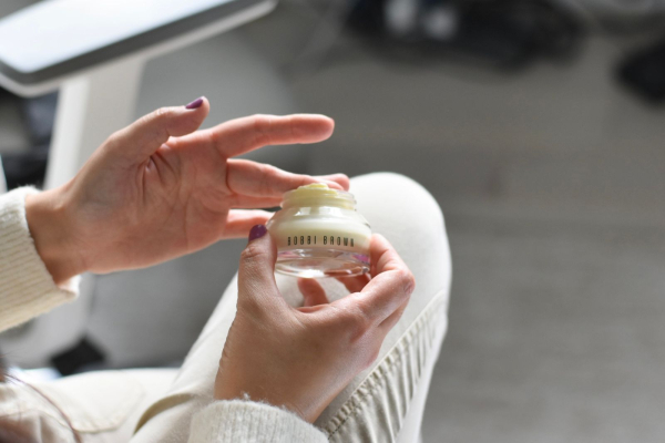 A photo of a woman dipping her finger into a jar of Bobbi Brown Vitamin Enriched Face Base